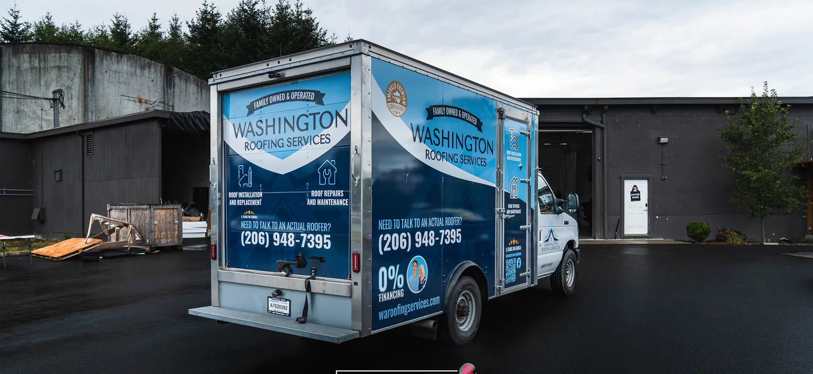 White box truck wrapped in blue graphics for a roofing company with a phone number and a 0% financing offer