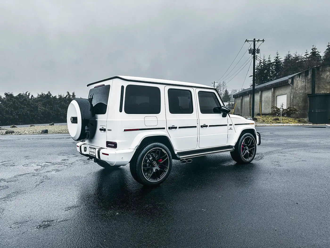 Mercedes-AMG G63 in a white color change wrap with black wheels and red brake calipers on wet pavement under gray skies