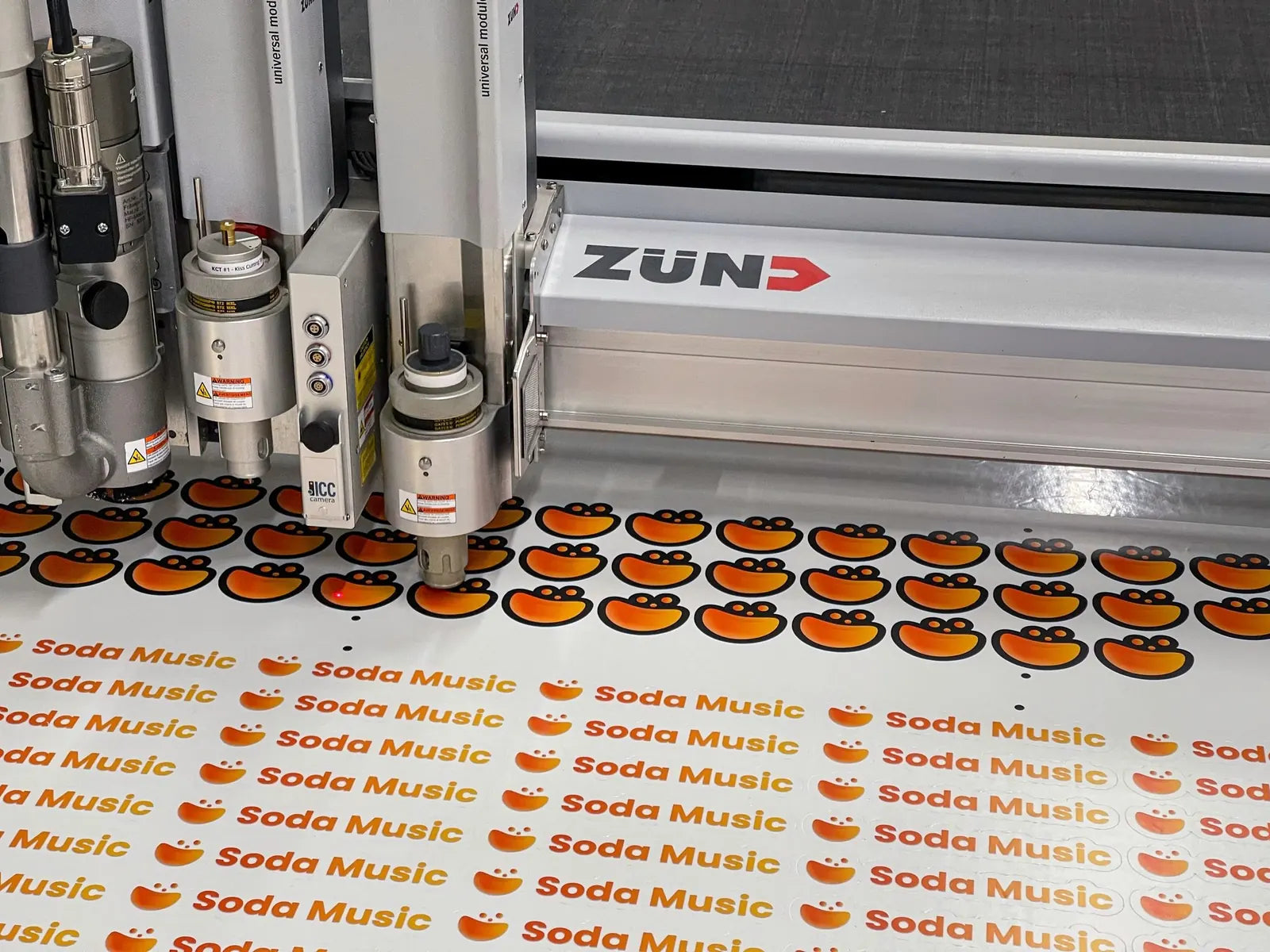 Zund digital cutter kiss-cutting a sheet of custom printed Soda Music logo stickers on the cutting table at Ardor Printing