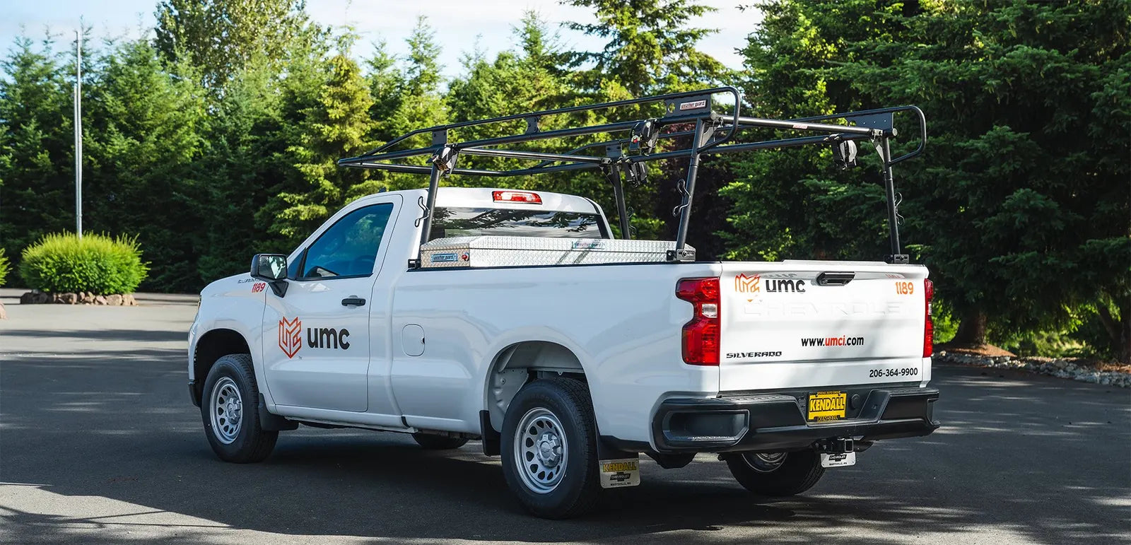 White Chevrolet Silverado work truck upfitted with a black ladder rack and crossover toolbox, with UMC fleet lettering