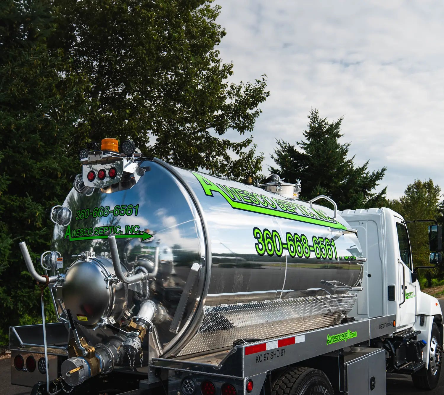Close-up of a polished stainless septic tank truck with green logo graphics and a large phone number on the tank