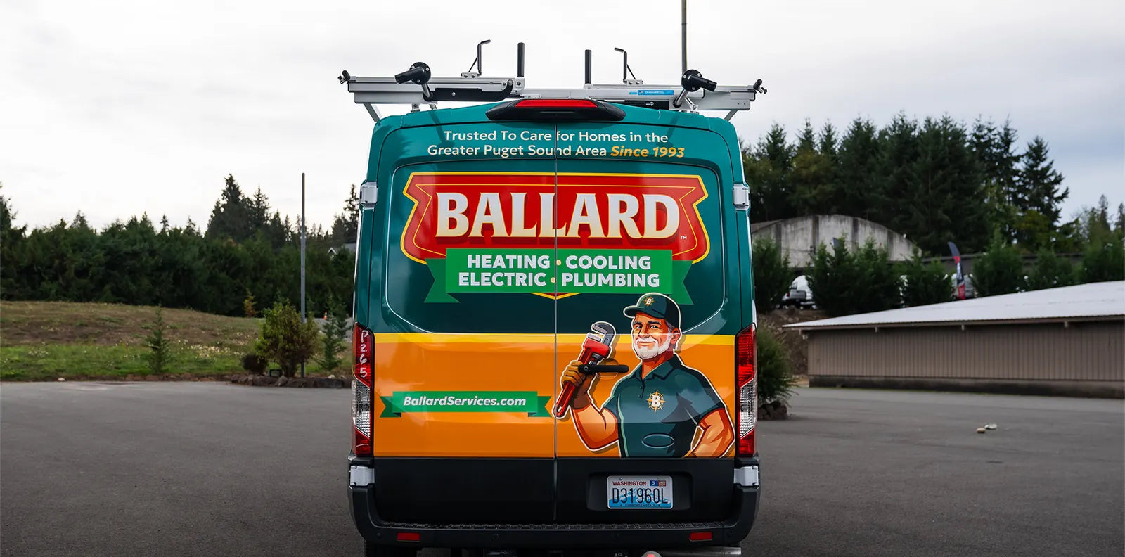 Rear of a Ford Transit work van wrapped with a plumber mascot, website address and a roof ladder rack
