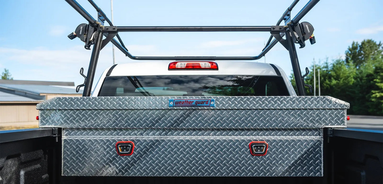 WEATHER GUARD diamond-plate aluminum crossover truck toolbox installed under a black ladder rack in a pickup bed