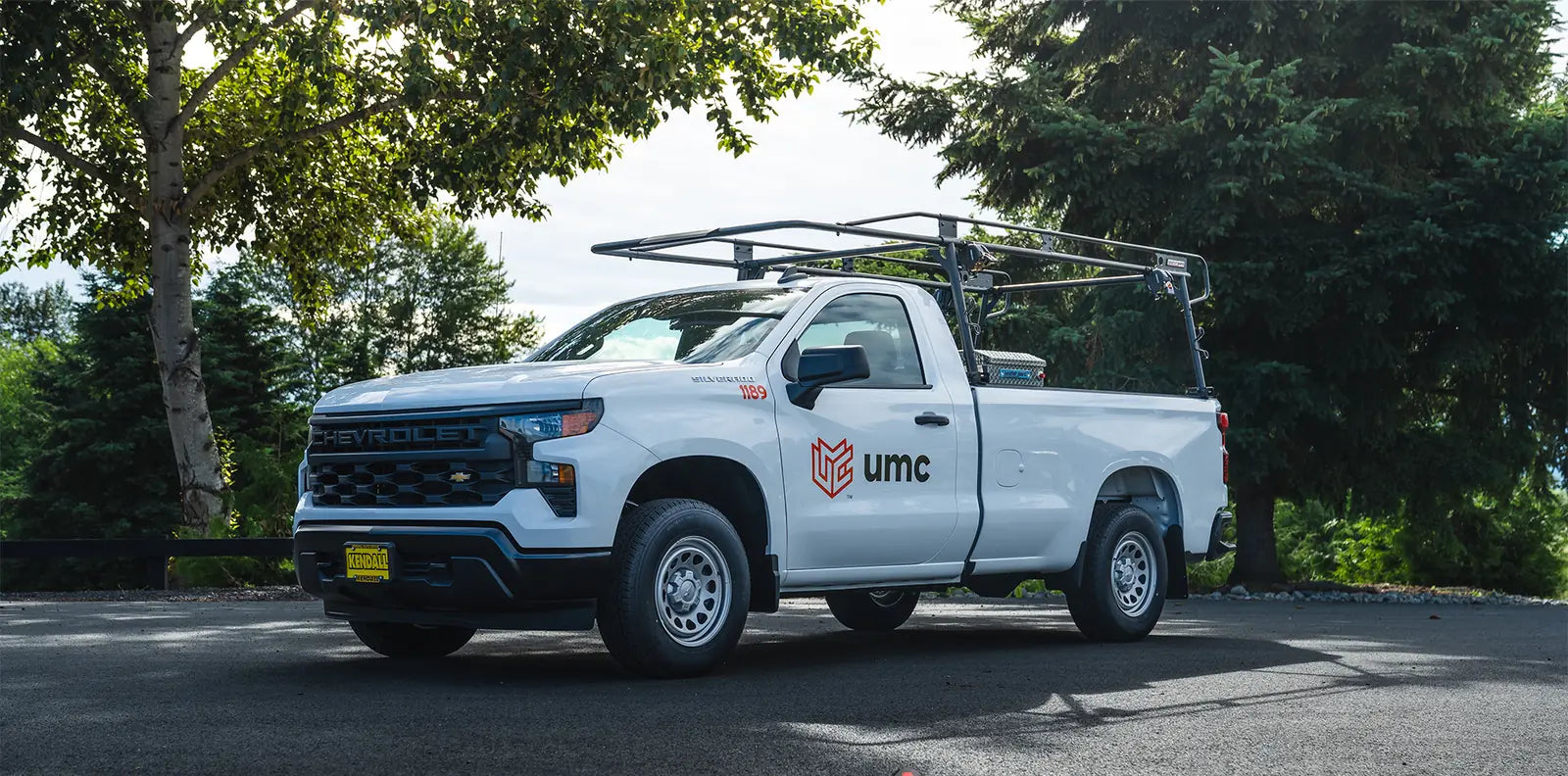 White Chevrolet Silverado work truck with a UMC door logo and a black ladder rack parked on asphalt