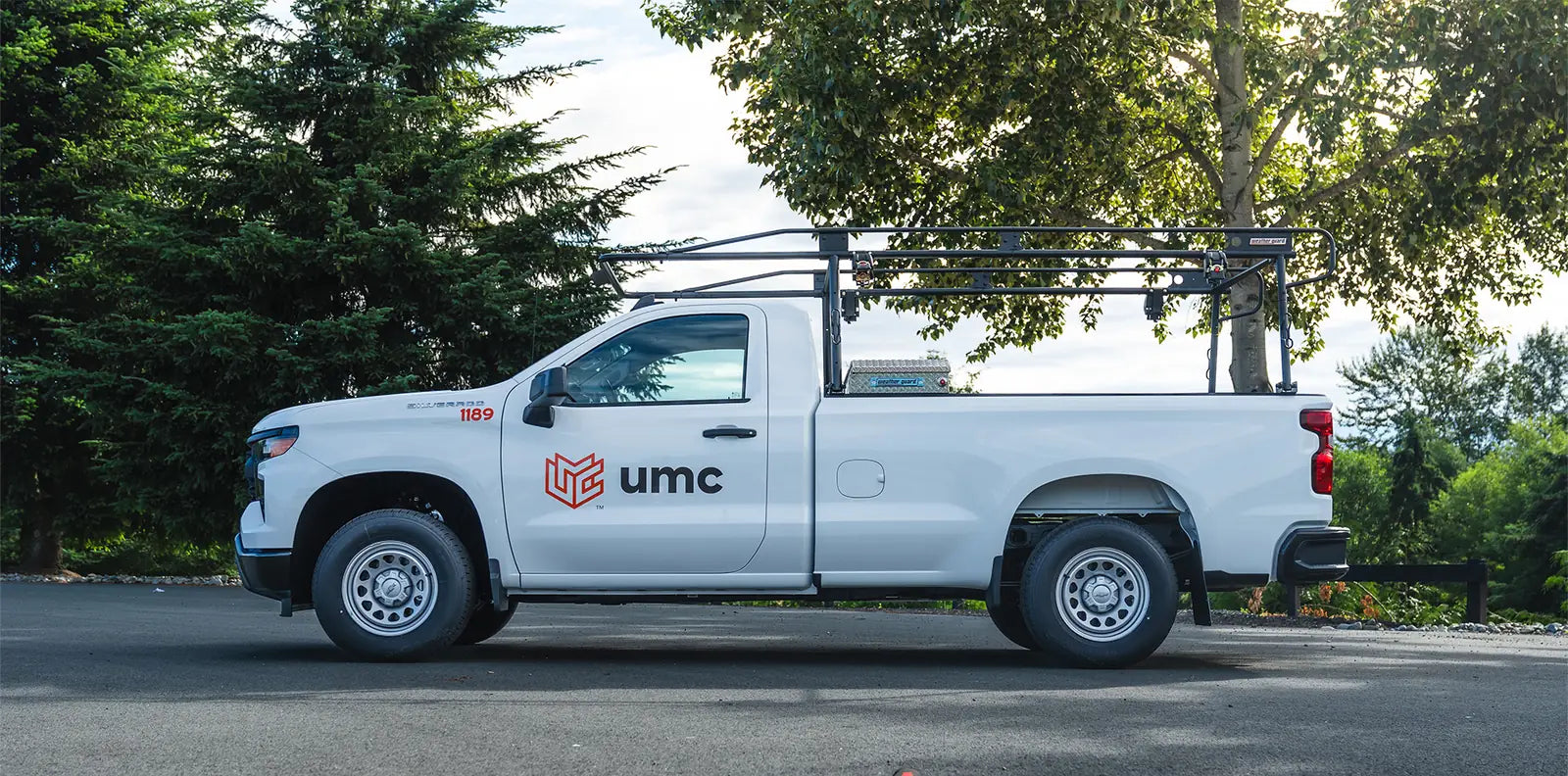 Side view of a white Chevrolet Silverado work truck with a black ladder rack and UMC door logo